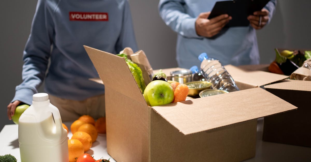 People packing a cardboard box with essentials like fruits, vegetables, and bottled water for charity.